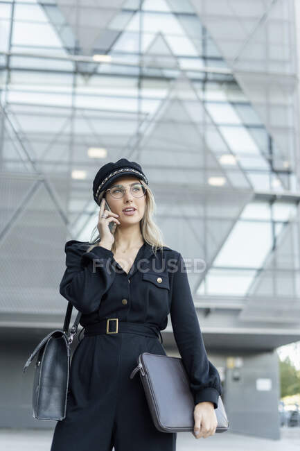 lógica gatito Verde Joven mujer de negocios rubia con gorra de marinero negro, bolsa para  portátil y teléfono inteligente — aire libre, En el teléfono - Stock Photo  | #467057232