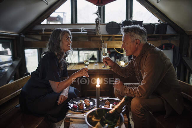 Старша пара вечеряє зі свічкою на човні в маяку, чіпляючи шампанські окуляри. — стокове фото