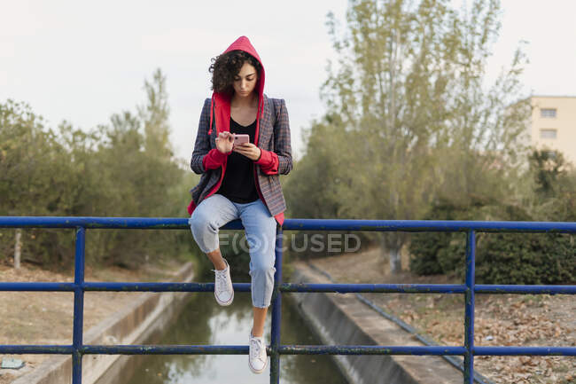 Young woman sitting on railing using mobile phone — Stock Photo