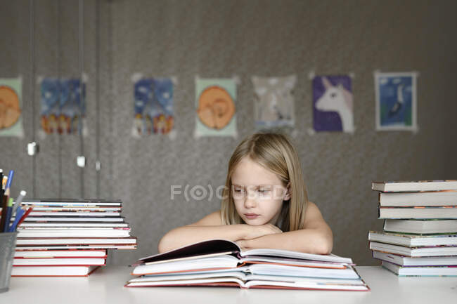 Chica sentada en la mesa en casa leyendo libros - foto de stock