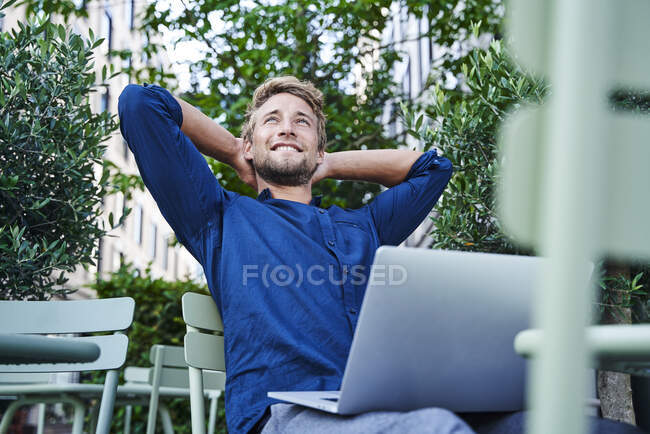 Jovem empresário com laptop em um café ao ar livre na cidade tendo uma pausa — Fotografia de Stock