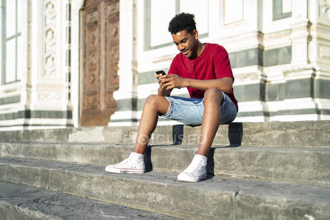 Молодий чоловік сидить на відкритих сходах, перевіряючи смартфон у Флоренції (Італія). — стокове фото