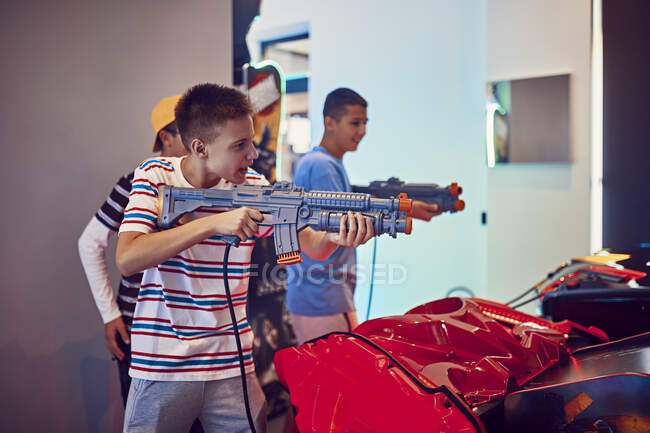 Adolescentes amigos atirando com armas em uma arcada de diversão — Fotografia de Stock