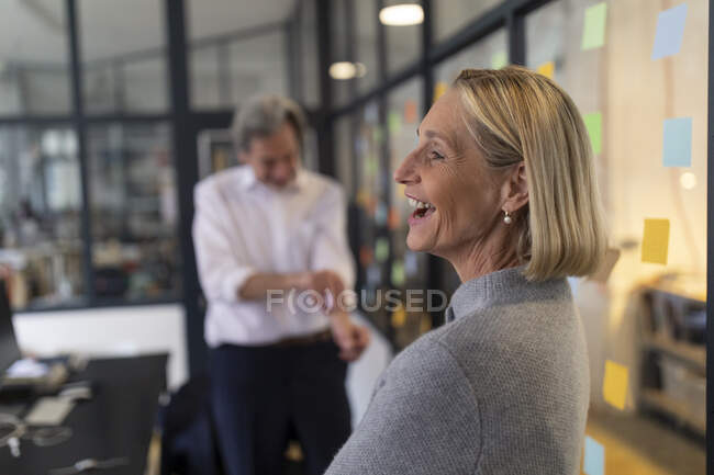 Empresária feliz com colega e notas pegajosas no painel de vidro no escritório — Fotografia de Stock