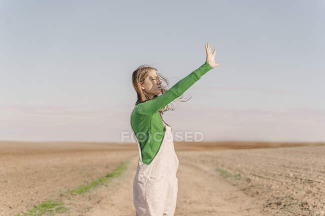 Young woman standing on dry field, shielding eyes — Stock Photo