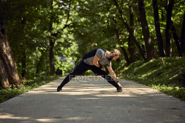 Sporty man stretching on forest path — Stock Photo