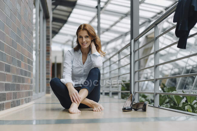 Portrait d'une femme d'affaires souriante assise par terre dans un bureau moderne — Photo de stock