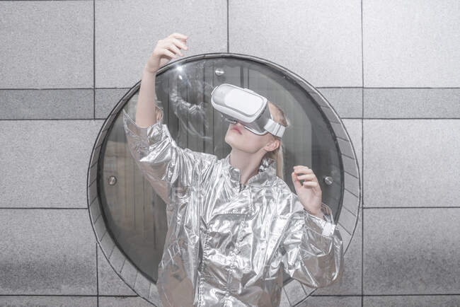 Дівчина в срібному костюмі дивиться через окуляри VR, спостерігаючи за її рукою — стокове фото