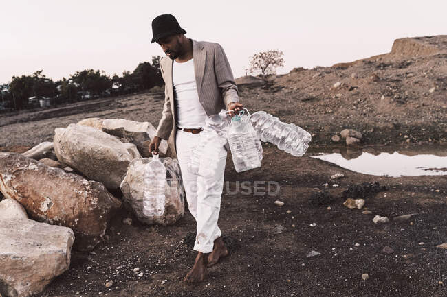 Young man walking in barren land holding empty plastic bottles — Stock Photo