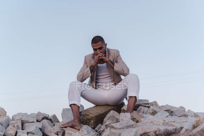 Aggressiver junger Mann sitzt auf Steinhaufen — Stockfoto