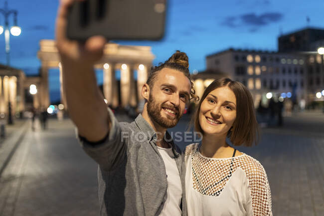 Coppia felice che si fa un selfie al cancello di Brandeburgo all'ora blu, Berlino, Germania — Foto stock