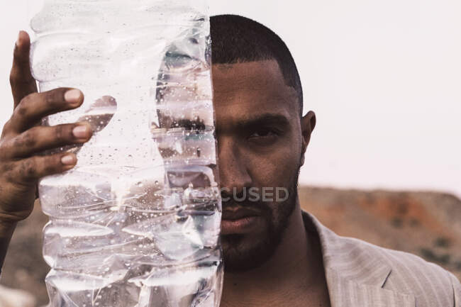 Portrait d'un jeune homme sérieux tenant une bouteille en plastique vide — Photo de stock
