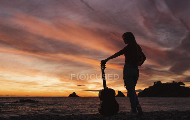 Silhouette de femme avec guitare debout sur la plage au coucher du soleil, Almunecar, Espagne — Photo de stock