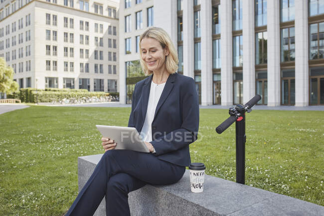 Donna d'affari seduta su un muro in città utilizzando tablet — Foto stock
