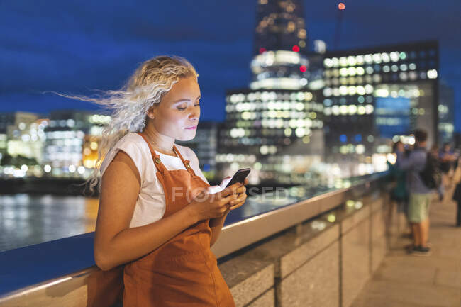 Jovem mulher na cidade ao entardecer olhando para seu smartphone — Fotografia de Stock