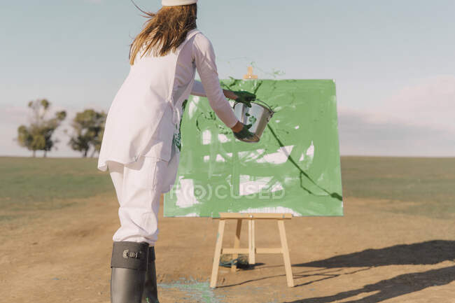 Jovem no campo seco, pintura de lona com tinta verde — Fotografia de Stock
