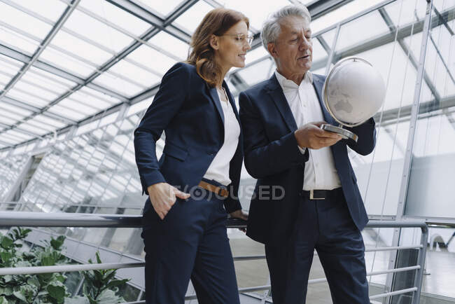 Hombre de negocios y mujer de negocios mirando el mundo en el moderno edificio de oficinas - foto de stock