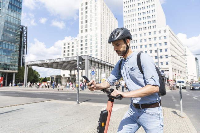 Uomo d'affari che guarda lo smartphone pendolarismo su scooter elettrico in città, Berlino, Germania — Foto stock