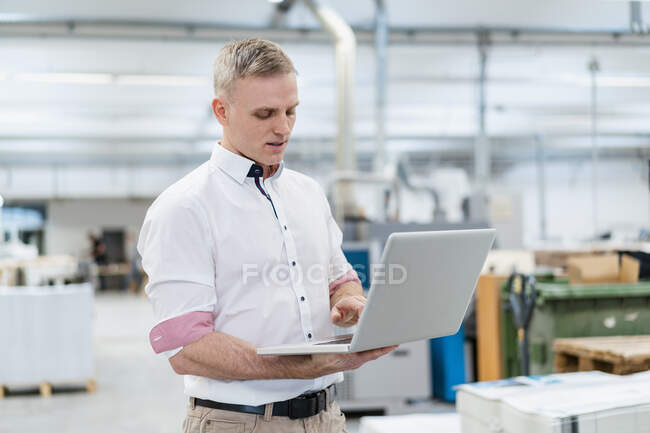 Businessman using laptop in factory — Stock Photo