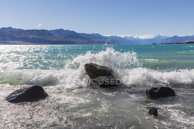 Nouvelle-Zélande, Océanie, Île du Sud, Canterbury, Ben Ohau, Lac Pukaki et Alpes du Sud (Nouvelle-Zélande Alpes) avec Aoraki / Mont Cook, Vagues éclaboussant contre les rochers — Photo de stock