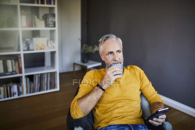 Entspannter älterer Mann zu Hause mit Handy und Tasse Kaffee — Stockfoto
