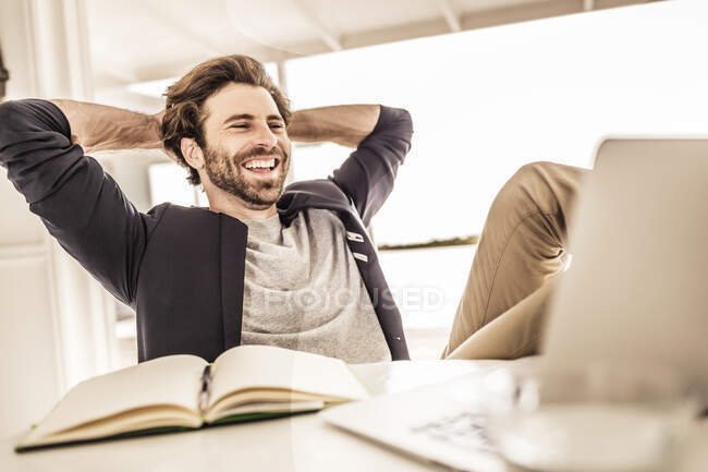 Rire jeune homme en veste d'affaires travaillant sur un ordinateur portable dans une maison de plage — Photo de stock