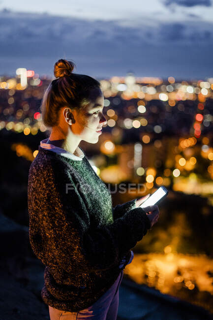 Jovem mulher sentada no corrimão acima da cidade usando telefone celular, Barcelona, Espanha — Fotografia de Stock