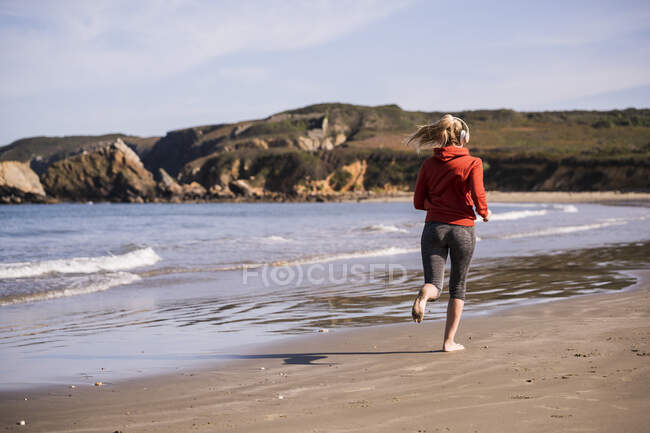 Corredor femenino en la playa con auriculares - foto de stock