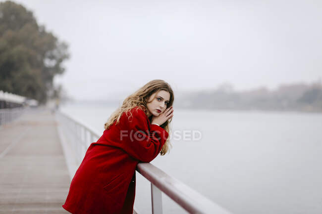 Ritratto di giovane donna vestita di rosso, appoggiata alla ringhiera nei giorni di pioggia — Foto stock