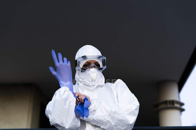 Female scientist wearing protective suit and mask and putting on protective gloves — Stock Photo