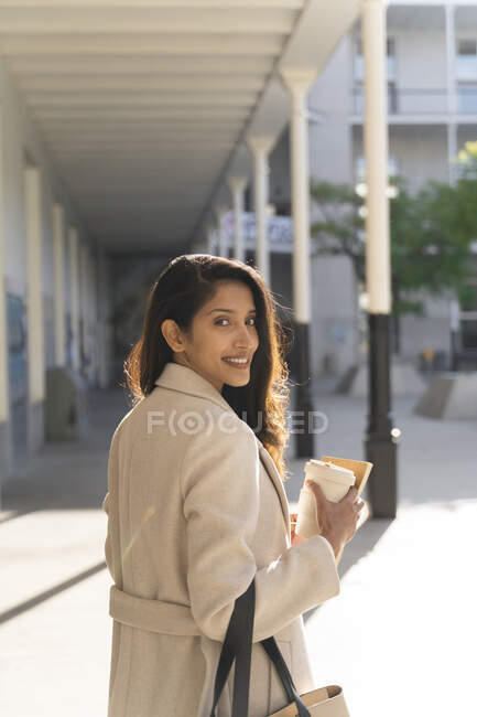 Retrato de una joven sonriente con libro y café para llevar en la ciudad - foto de stock
