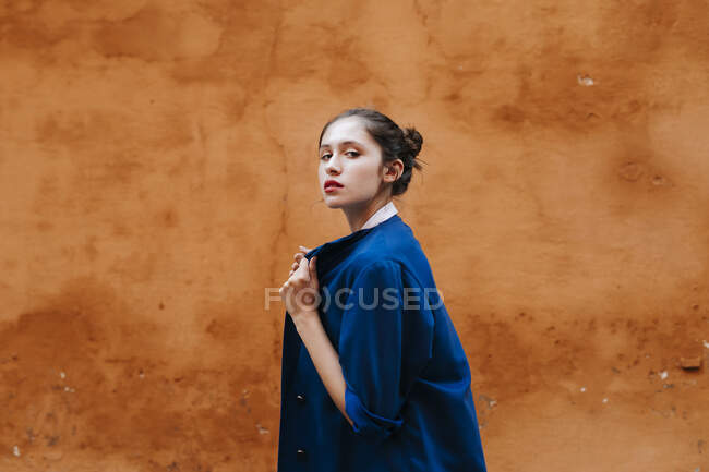 Portrait of female teenager wearing blue jacket in front of a brown wall — Photo de stock