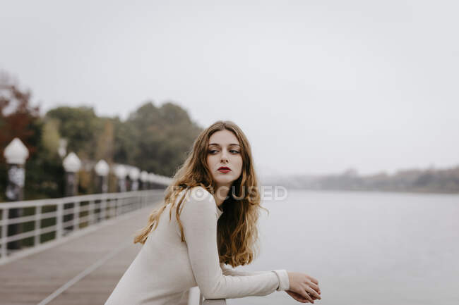 Portrait de jeune femme vêtue d'une robe blanche, appuyée sur une rampe le jour de la pluie — Photo de stock