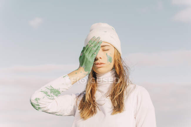 Mujer joven cubriendo el ojo con la mano verde - foto de stock
