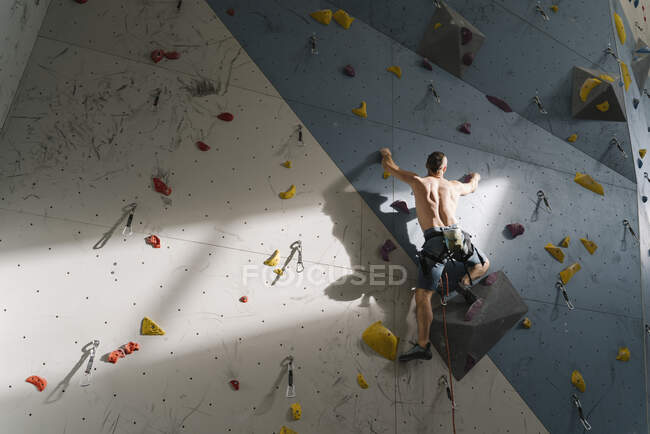 Uomo senza maglietta che si arrampica sulla parete in palestra di arrampicata — Foto stock