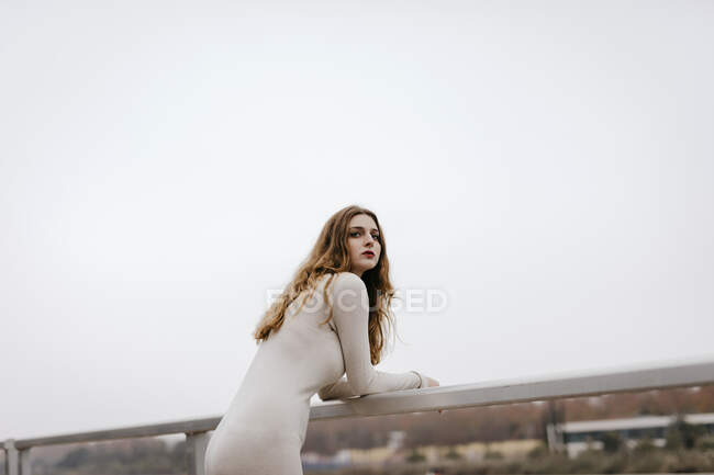Porträt einer jungen Frau in weißem Kleid, die sich bei Regen an ein Geländer lehnt — Stockfoto