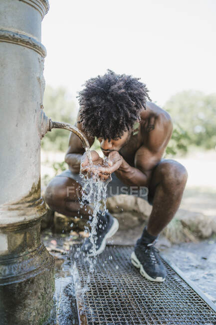 Jeune homme pendant l'entraînement, boire à la fontaine dans un parc — Photo de stock