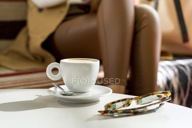 Lunettes et tasse à café sur la table dans un café avec une femme en arrière-plan — Photo de stock