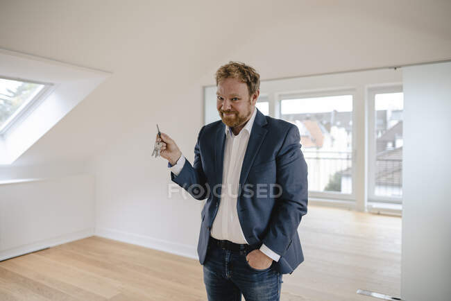 Portrait of smiling businessman standing in empty apartement holding key — Stock Photo