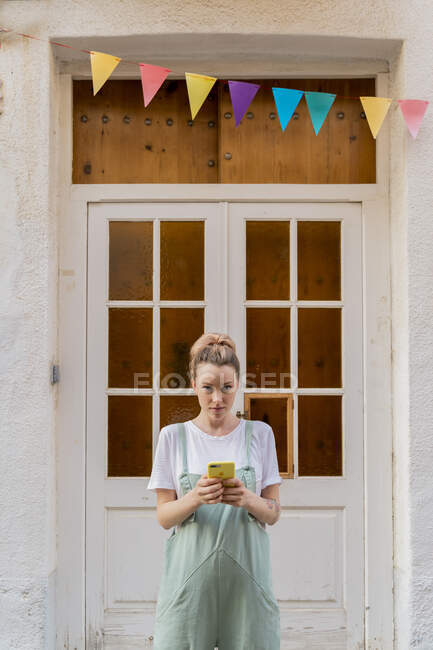 Portrait of young woman with smartphone standing in front of wooden door — Stock Photo