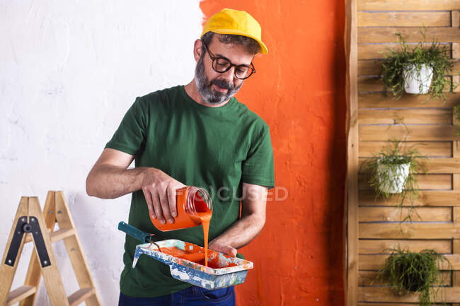 Homem derramando tinta laranja na bandeja de pintura — Fotografia de Stock
