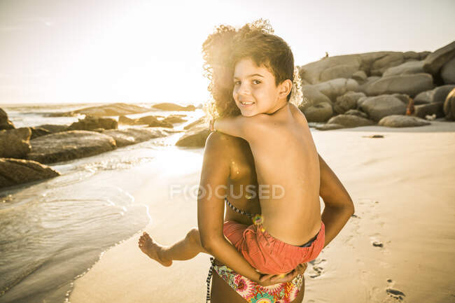 Mutter trägt ihren lächelnden Sohn huckepack am Strand — Stockfoto