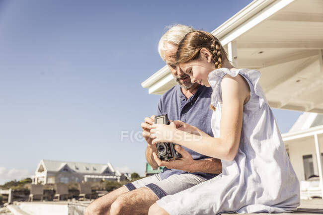 Pai e filha sentados no terraço em sol examinando câmera vintage — Fotografia de Stock