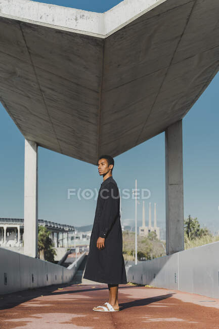 Молодой человек в черном кафтане стоит на пешеходном мосту — стоковое фото
