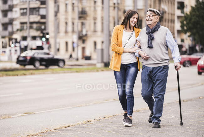 Nipote adulta che assiste il nonno passeggiando con bastone da passeggio — Foto stock