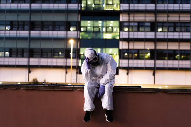 Female scientist wearing protective suit and mask sitting in front of a laboratory — Stock Photo