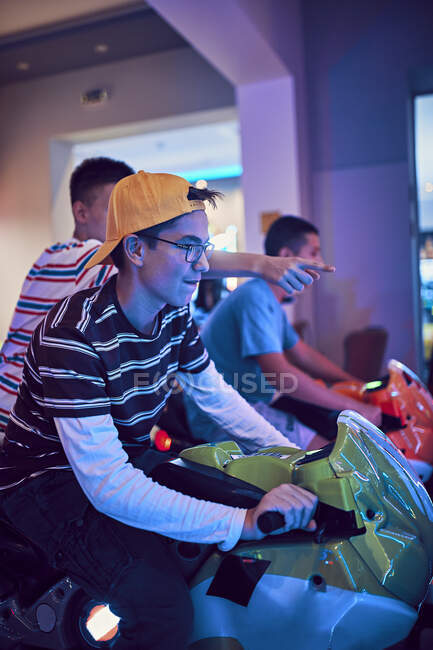 Amis adolescents jouant avec un simulateur de conduite dans une arcade de divertissement — Photo de stock