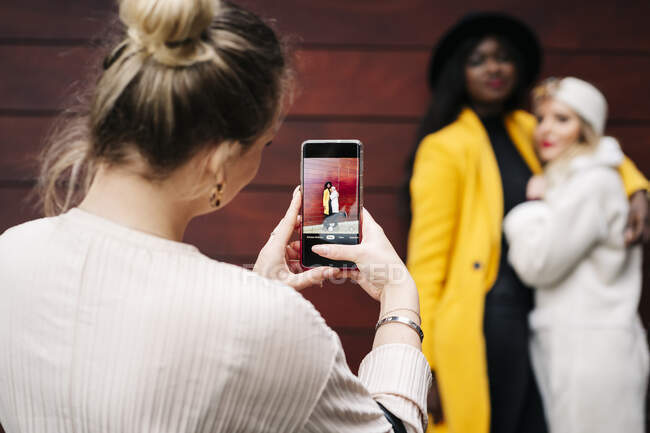 Жінка фотографує з мобільним телефоном двох друзів. — стокове фото