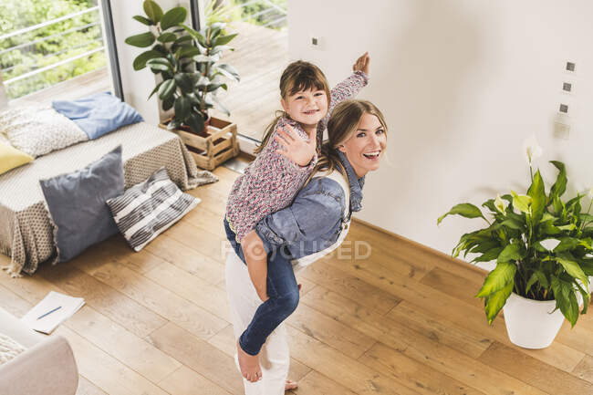 Mère heureuse portant fille piggyback à la maison — Photo de stock