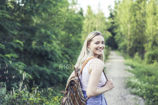 Portrait of smiling young woman with backpack on forest track — Stock Photo